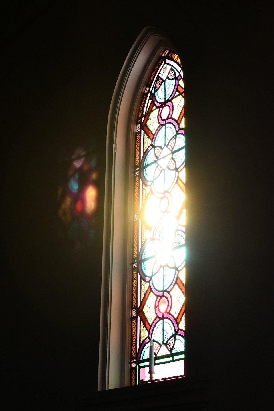 Sunlight streams through a colorful arched stained glass window.