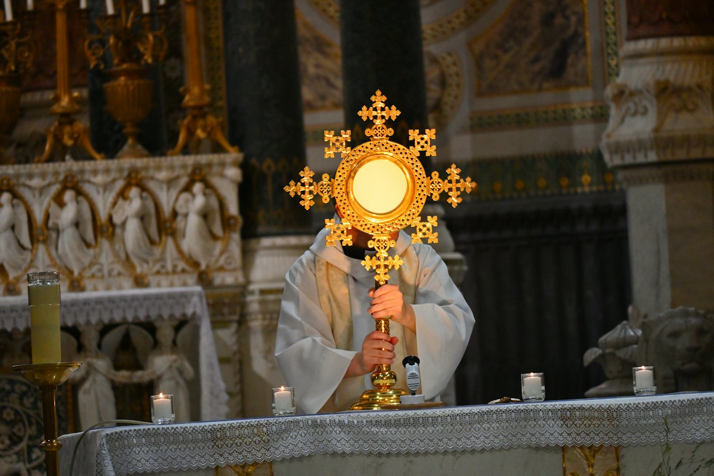 A priest holds a golden monstrance during a religious ceremony.