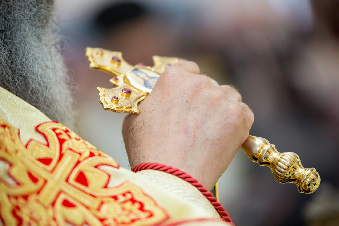 Cleric holding a golden cross with red stones and an icon.