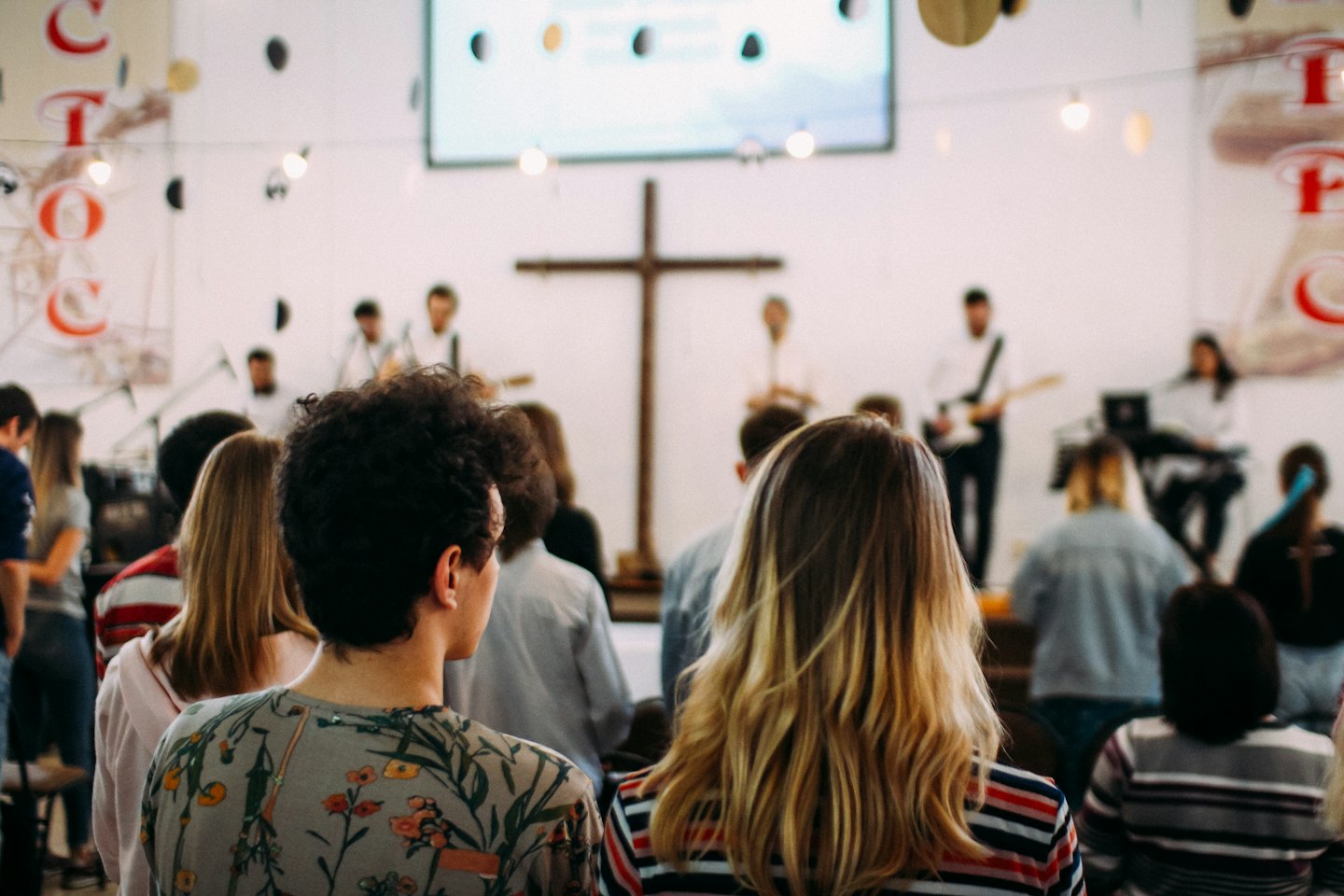 Congregation members watch a band perform on stage beneath a wooden cross.