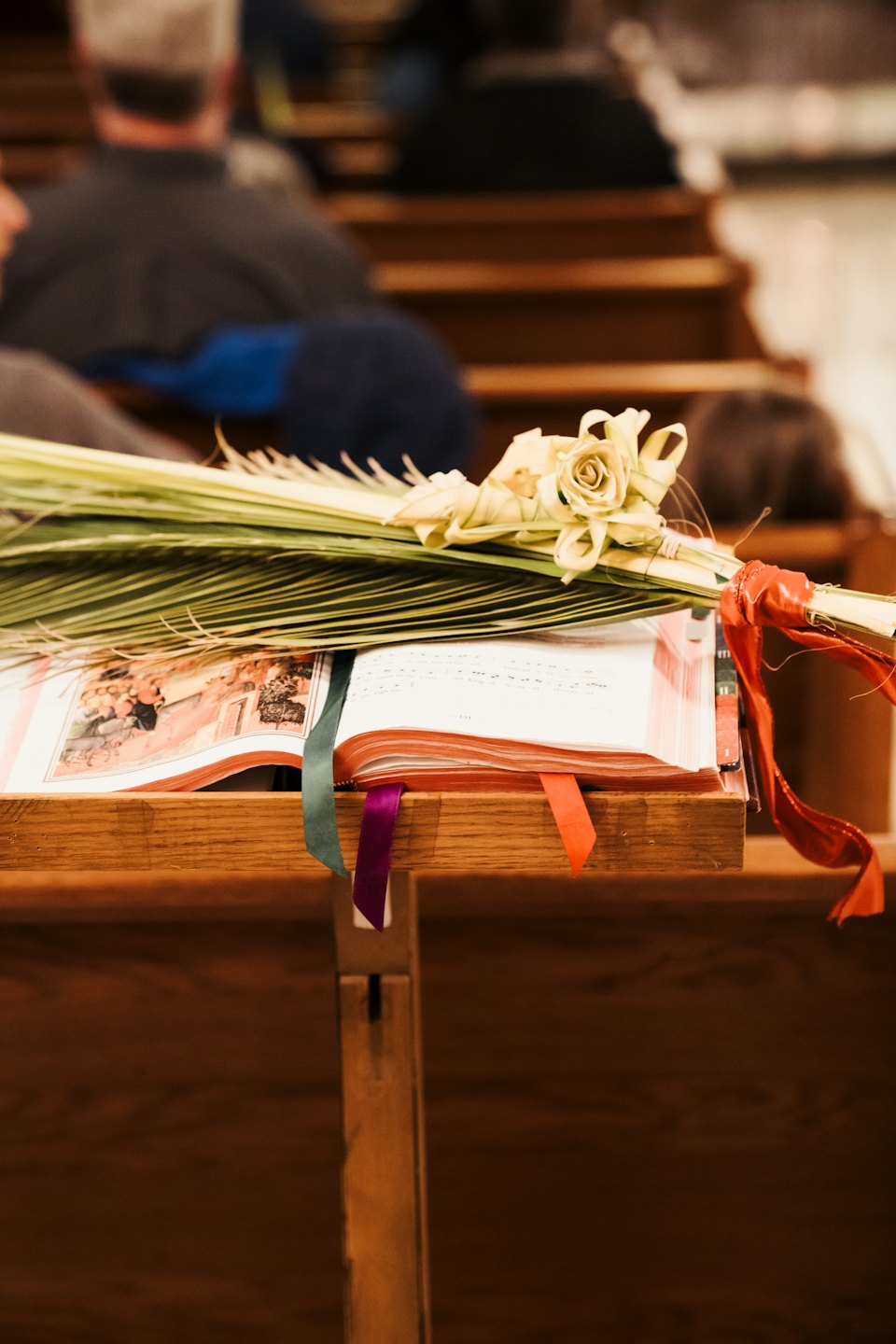 Open prayer book and palm fronds rest on a wooden pew.