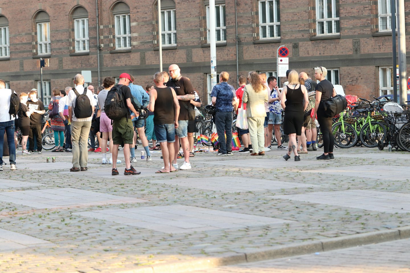 People chatting on a plaza near parked bicycles and a brick building.